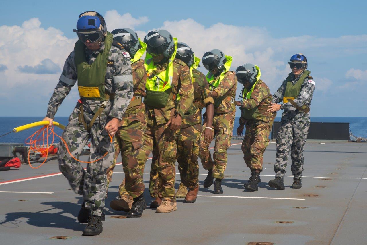 Members of the Papua New Guinea Defence Force Maritime Element are escorted off the flight deck of HMAS Choules after being winched down to the deck from an MRH-90 Multi Role Helicopter during a deployment to the South West Pacific region